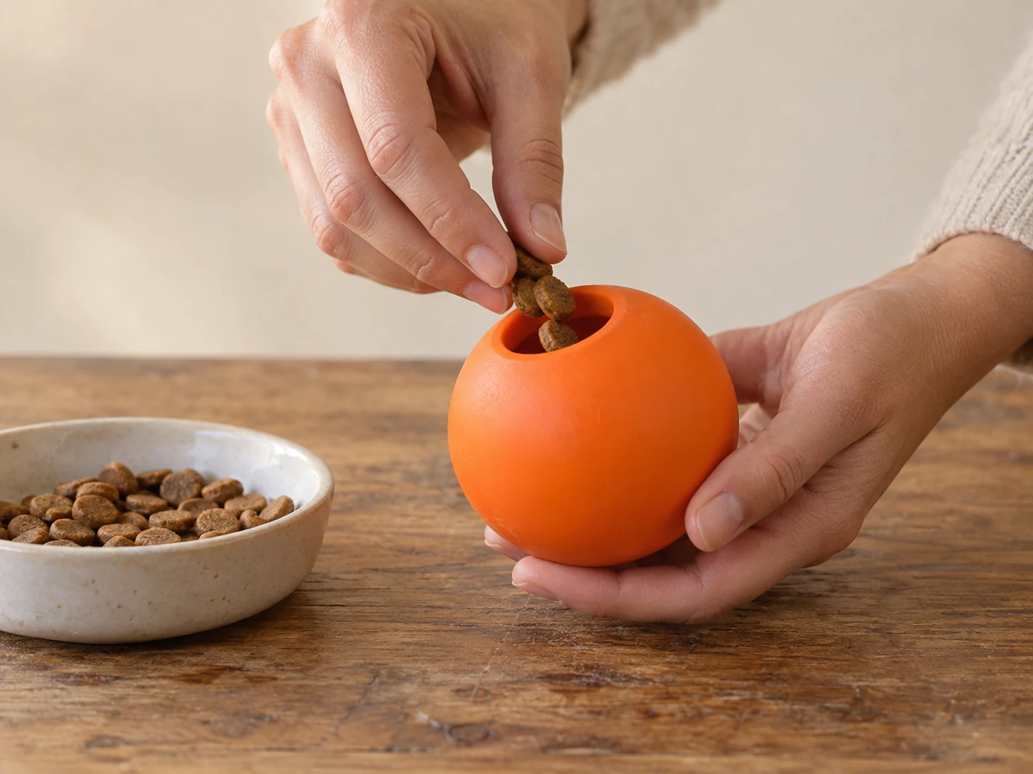 Hands placing a few dry kibble pieces into the wide opening of a generic hollow rubber toy
